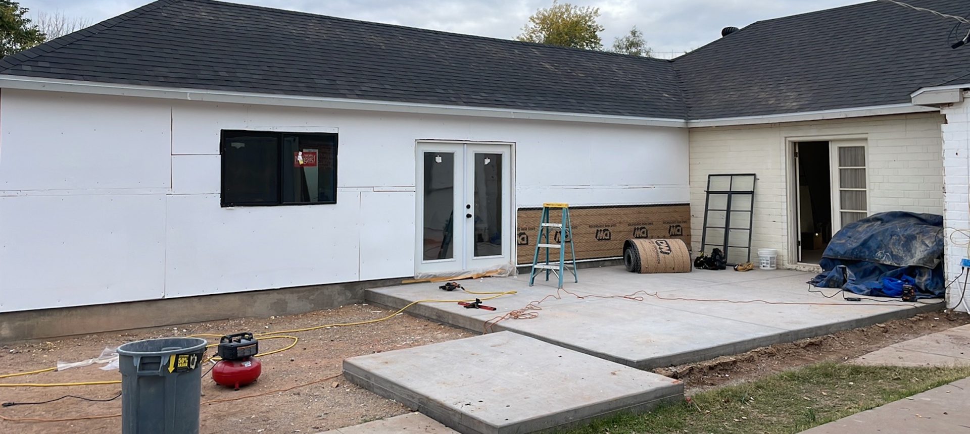 A partially constructed patio outside a white building with a ladder and construction materials.