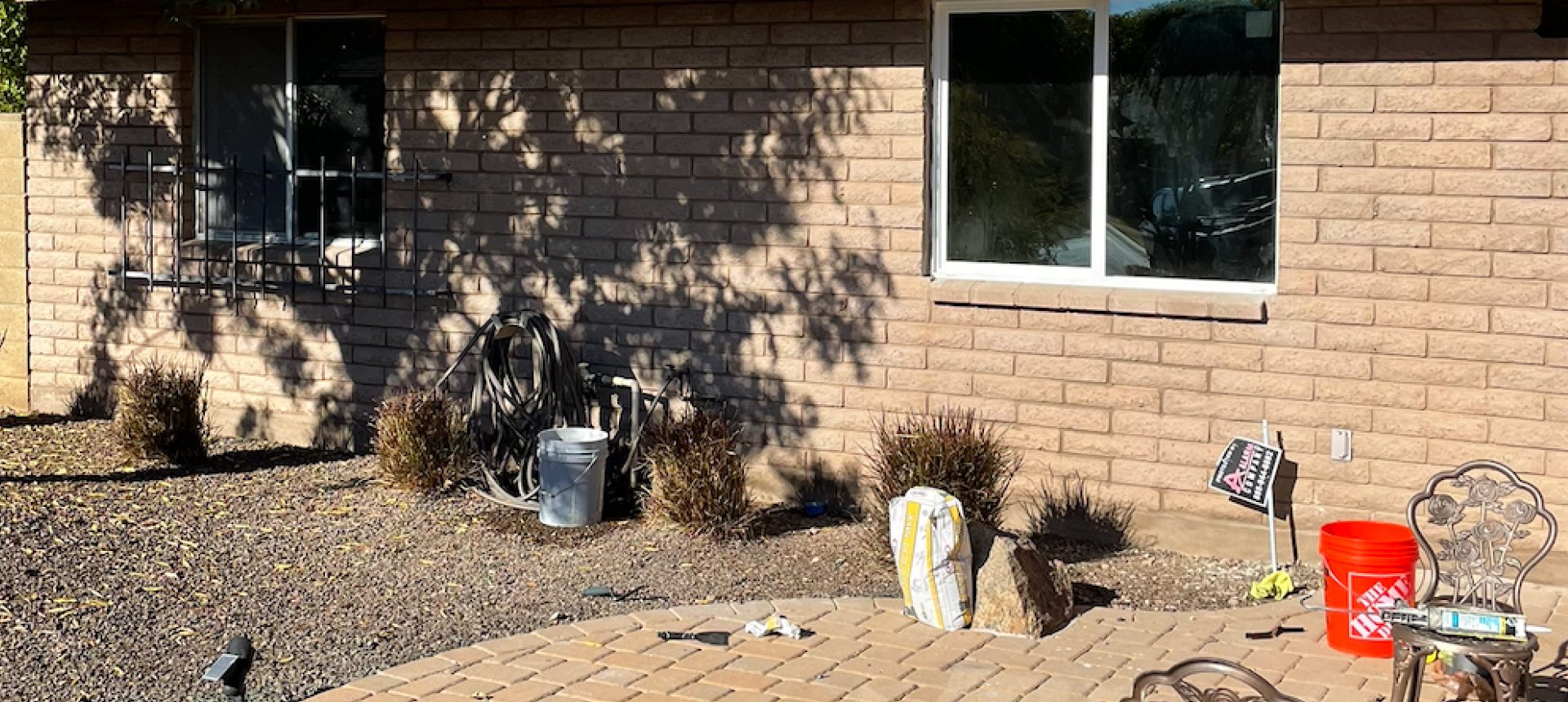 A cat resting in the shadow by a brick wall near a window.