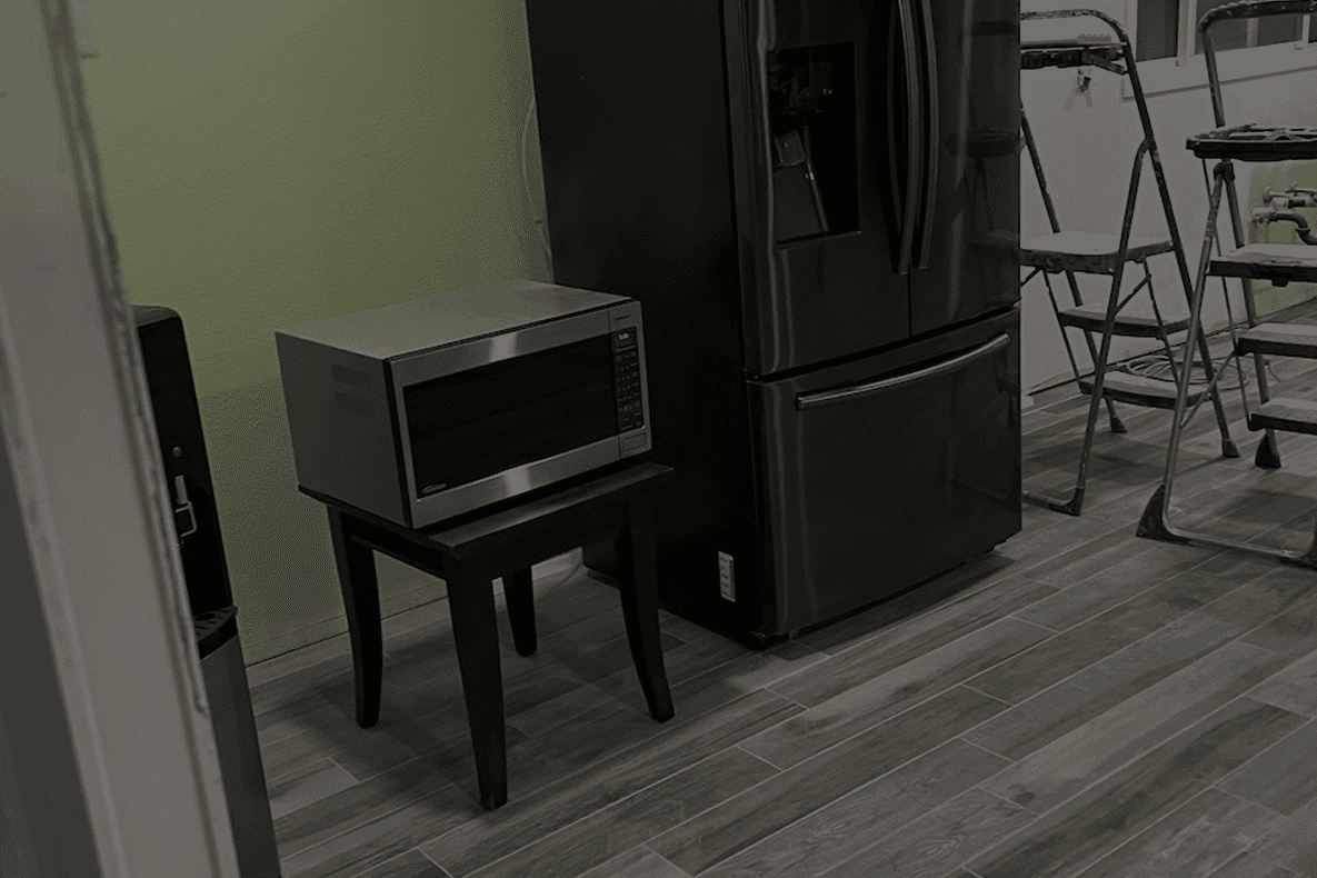 Compact microwave oven on a small table next to a black refrigerator in a kitchen.