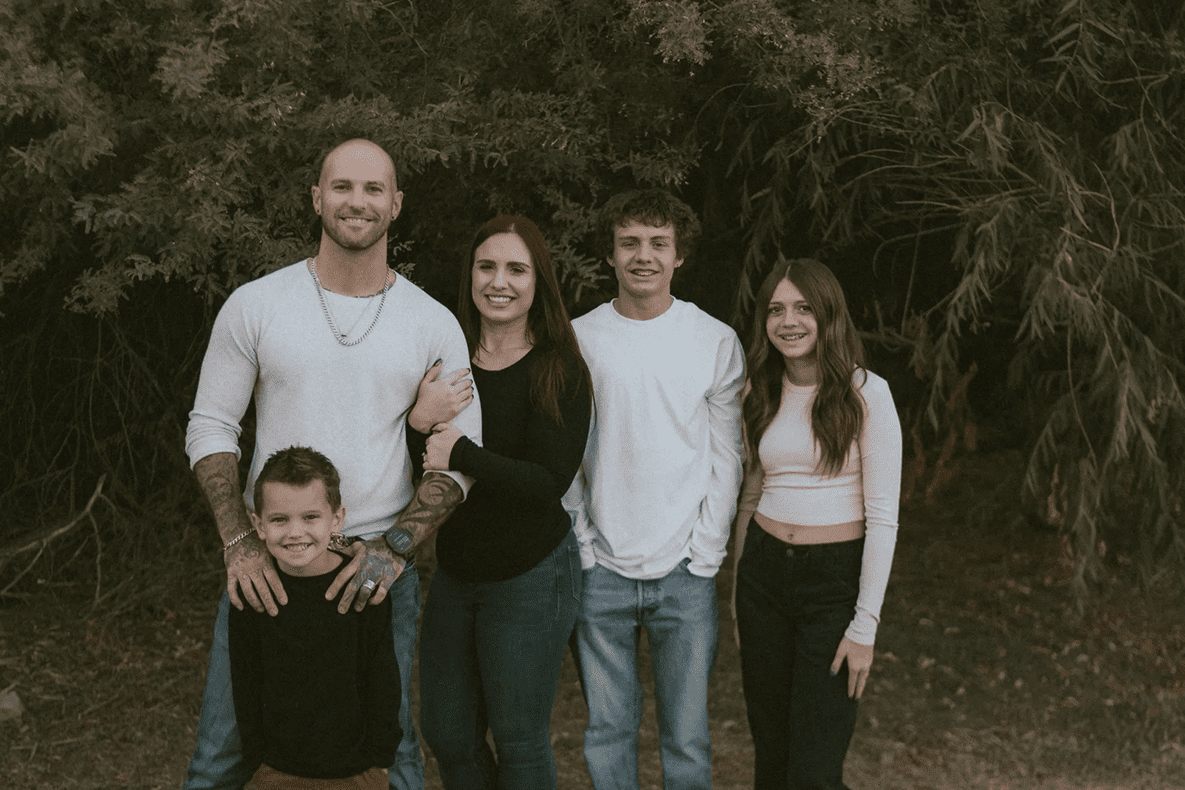 A happy family of five posing outdoors in casual clothing.